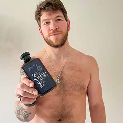 Man holds Particle Men's Formula shampoo bottle in his right hand.