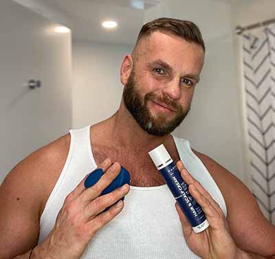 Man holding Particle hair grooming products, smiling in a bathroom.