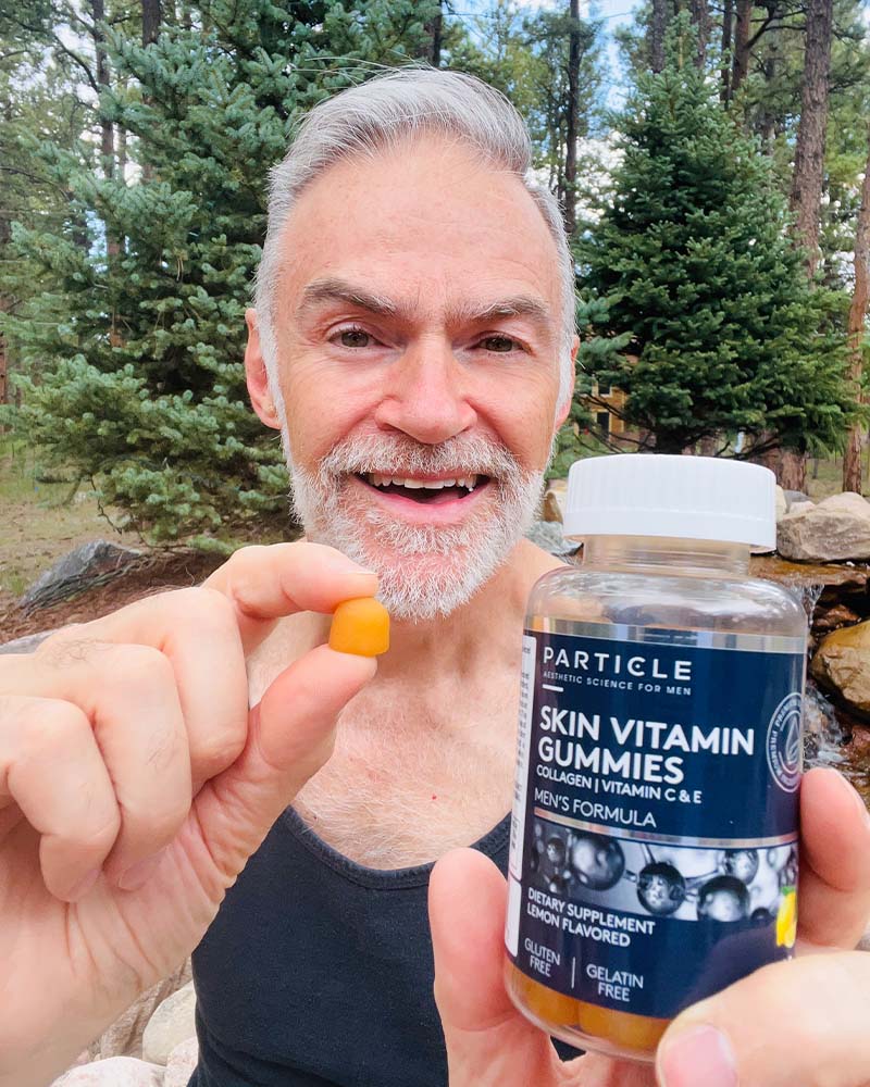 Man holding a Particle Skin Vitamin Gummies bottle in one hand and a single gummy in the other