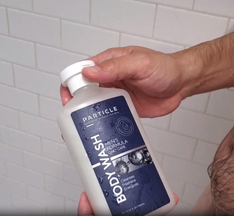 Hand holding bottle labeled Particle Body Wash in shower